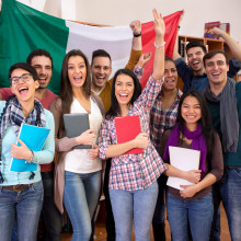 Smiling students with raised hands in front of Italian flag.