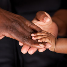 A picture of the hands of a baby, a young person and an older person holding hands