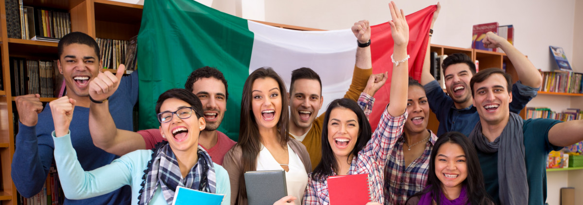 Smiling students with raised hands in front of Italian flag.