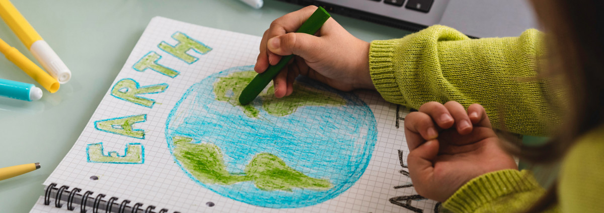 A little girl draws the earth with wax colors on school notebook for Earth Day.